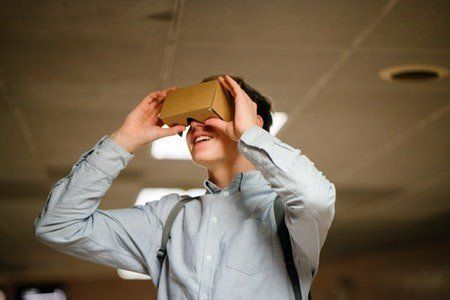 A man is wearing a cardboard virtual reality headset.